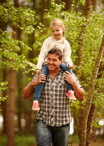 Dad and daughter walking through woods, daughter on shoulders.